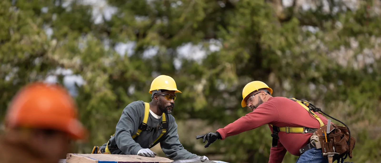 Two roofers in hard hats and safety harnesses working on a roof